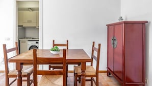 A dining area with a wooden table, four chairs, a red cabinet, and a kitchen in the background.