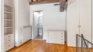 A room with a wooden floor, white walls, a radiator, a wardrobe, and a staircase.