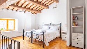 A bedroom with a wooden ceiling, a metal bed frame, a white bedside table, a white wardrobe, and a window with a view.