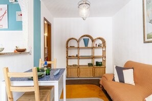 Una habitación con una mesa de comedor, sillas, un sofá, un estante de ratán y una lámpara colgante.