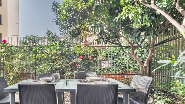Un espace de restauration en plein air, avec une table et des chaises, entouré de verdure et délimité par une clôture.