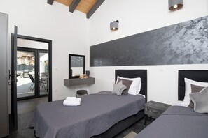 Two beds with grey bedding and a dark headboard, complemented by a large abstract painting and a sliding glass door to an outdoor patio.