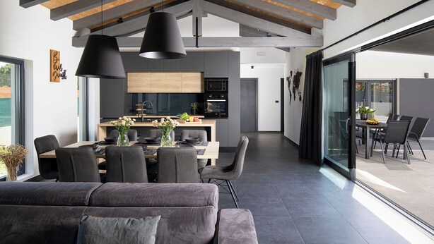 A modern interior with a dining area, kitchen, and a large sliding glass door leading to an outdoor patio. - Villa Frola (Istria - Muntic) (Muntic)