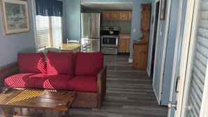 Ein kompakter Wohnraum mit rotem Sofa, Holz-Couchtisch und Küchenzeile, inklusive Kühlschrank, Backofen und Schränken.