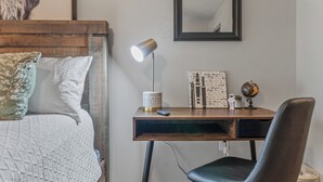 Un dormitorio con cabecera de madera, cama con ropa de cama blanca, escritorio con lámpara, un globo terráqueo y una cita enmarcada en la pared.