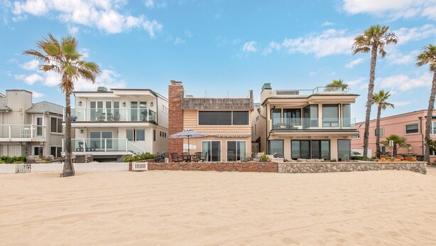Una propiedad frente a la playa con casas modernas, una playa arenosa y palmeras.
