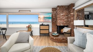 Una sala de estar con chimenea de ladrillo, un ventanal con vista a la playa y un rincón de descanso acogedor.
