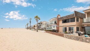 Una propiedad frente a la playa con arena, una hilera de casas con balcones y un cielo azul despejado.