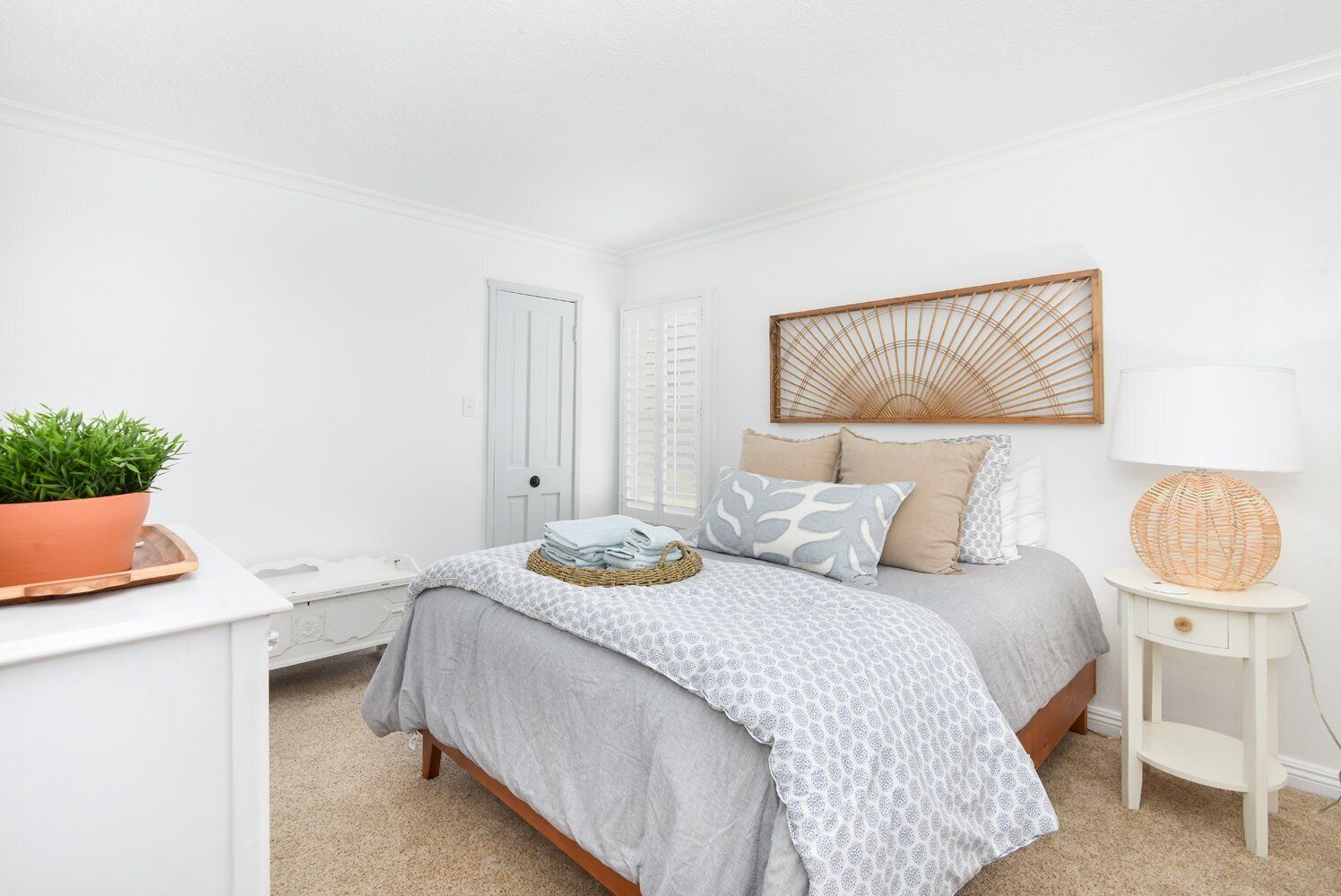 A bedroom with a bed, bedside table, lamp, and a potted plant.