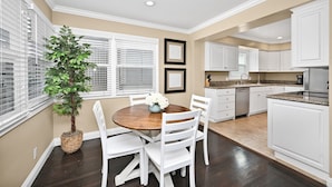 A kitchen with white cabinets, a wooden dining table, and a potted plant.