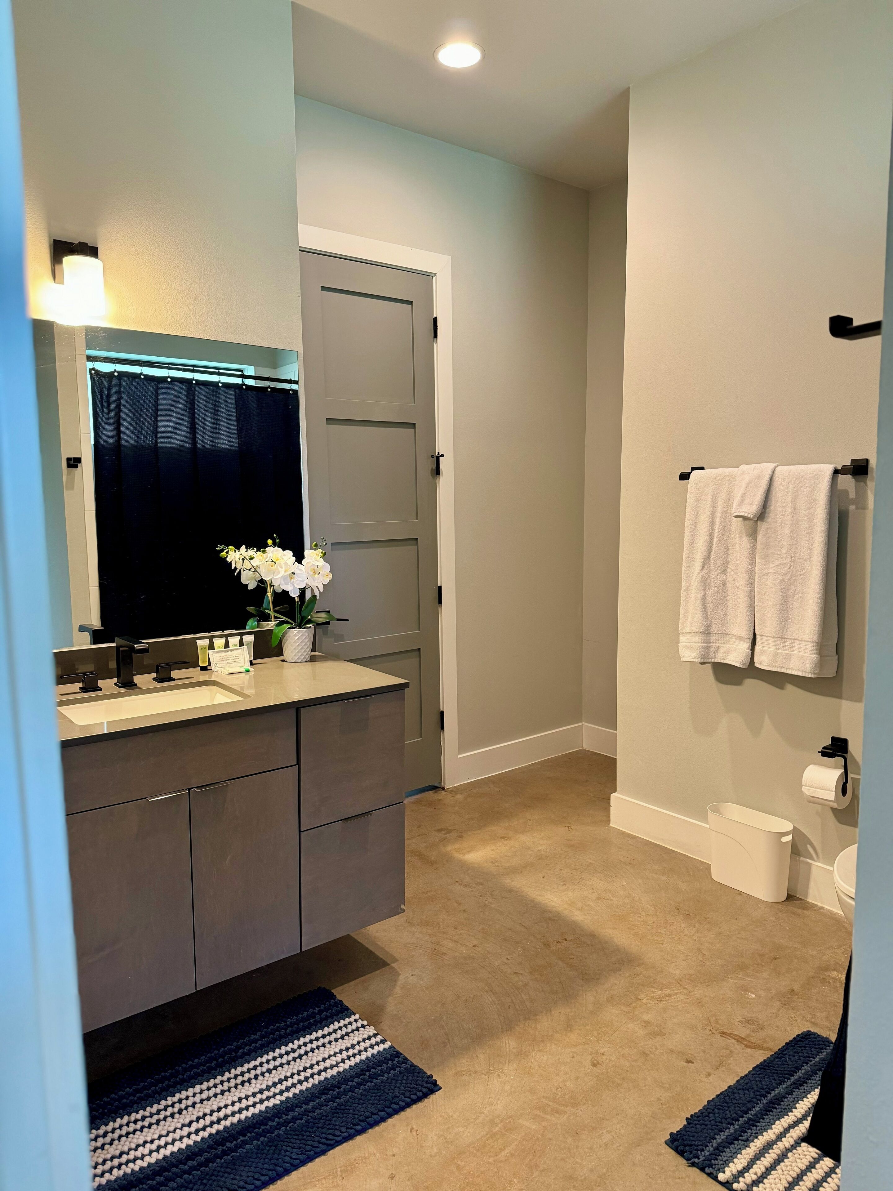 Un baño moderno con tocador gris oscuro, un espejo grande, un perchero y un inodoro.