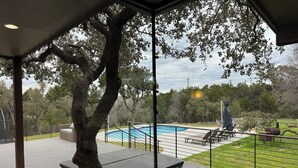 Eine moderne Außenterrasse mit Glasveranda, einem Swimmingpool und einer Rasenfläche mit Gartenmöbeln.