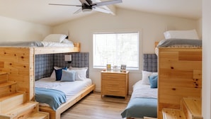 Habitación tipo dormitorio con literas, una escalera de madera, ventilador de techo y ventana con persianas.