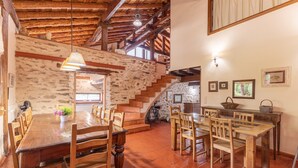 Un interno rustico con un tavolo da pranzo in legno, sedie, una parete in pietra e una scala.