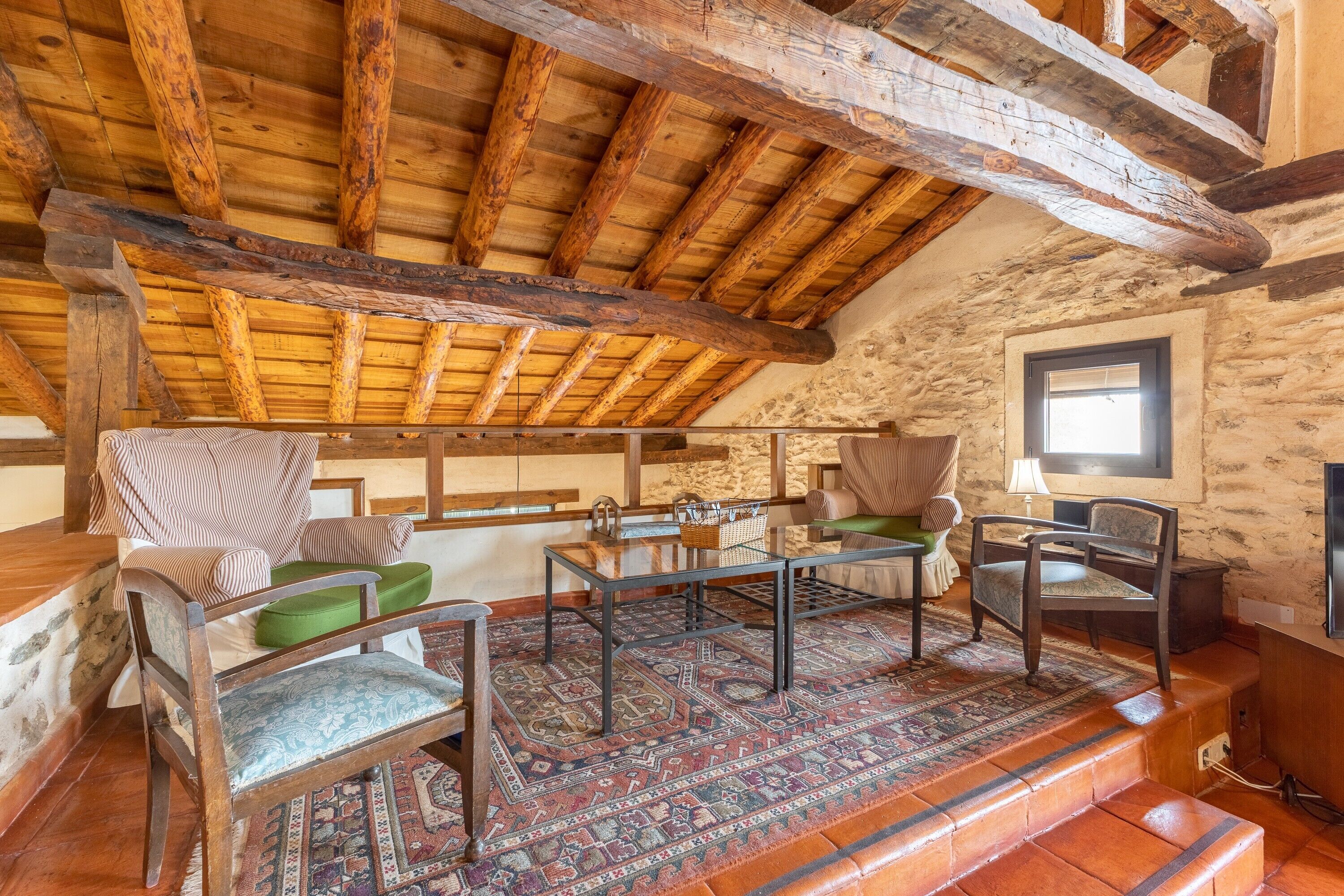 A rustic room with wooden beams, a stone wall, a patterned rug, and traditional furniture.