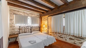 Una stanza con due letti, pareti in pietra, travi in legno e una finestra con tende.
