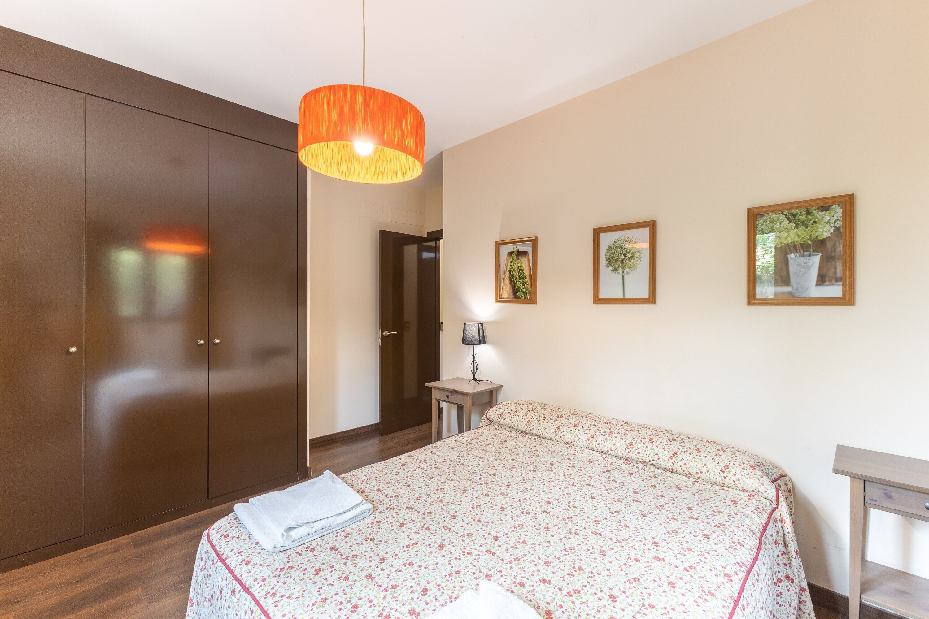 A bedroom with a bed, a wardrobe, a lamp, and framed pictures on the wall.