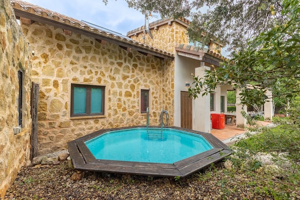 A stone building with a swimming pool, a wooden deck, and a red trash bin.