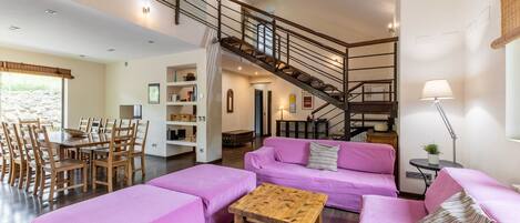 Amplia sala de estar con escalera, una mesa de comedor con sillas y un conjunto de sofás.