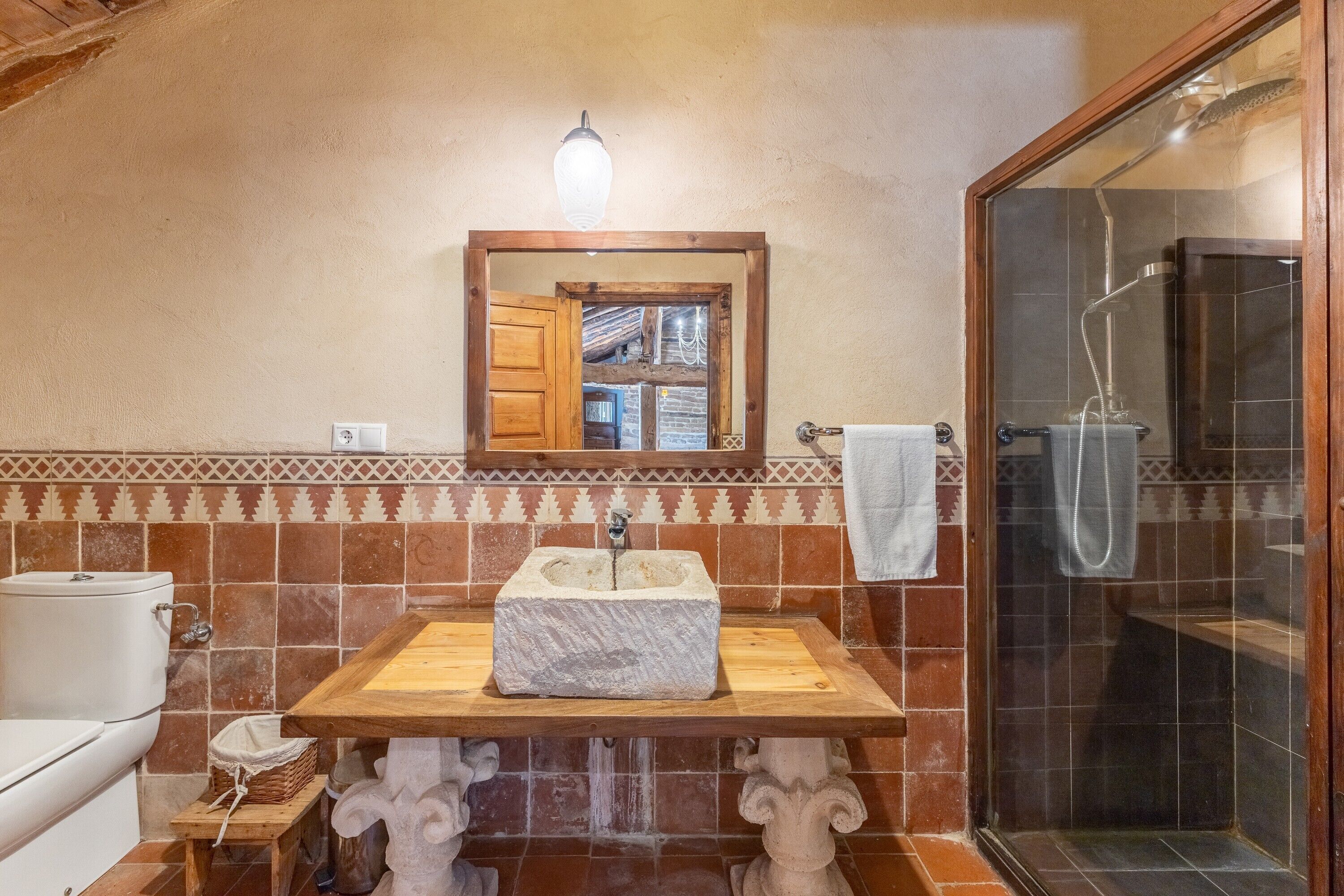 A bathroom with a stone sink, wooden vanity, a mirror, and a shower enclosure.