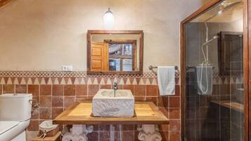 A bathroom with a stone sink, wooden vanity, a mirror, and a shower enclosure.