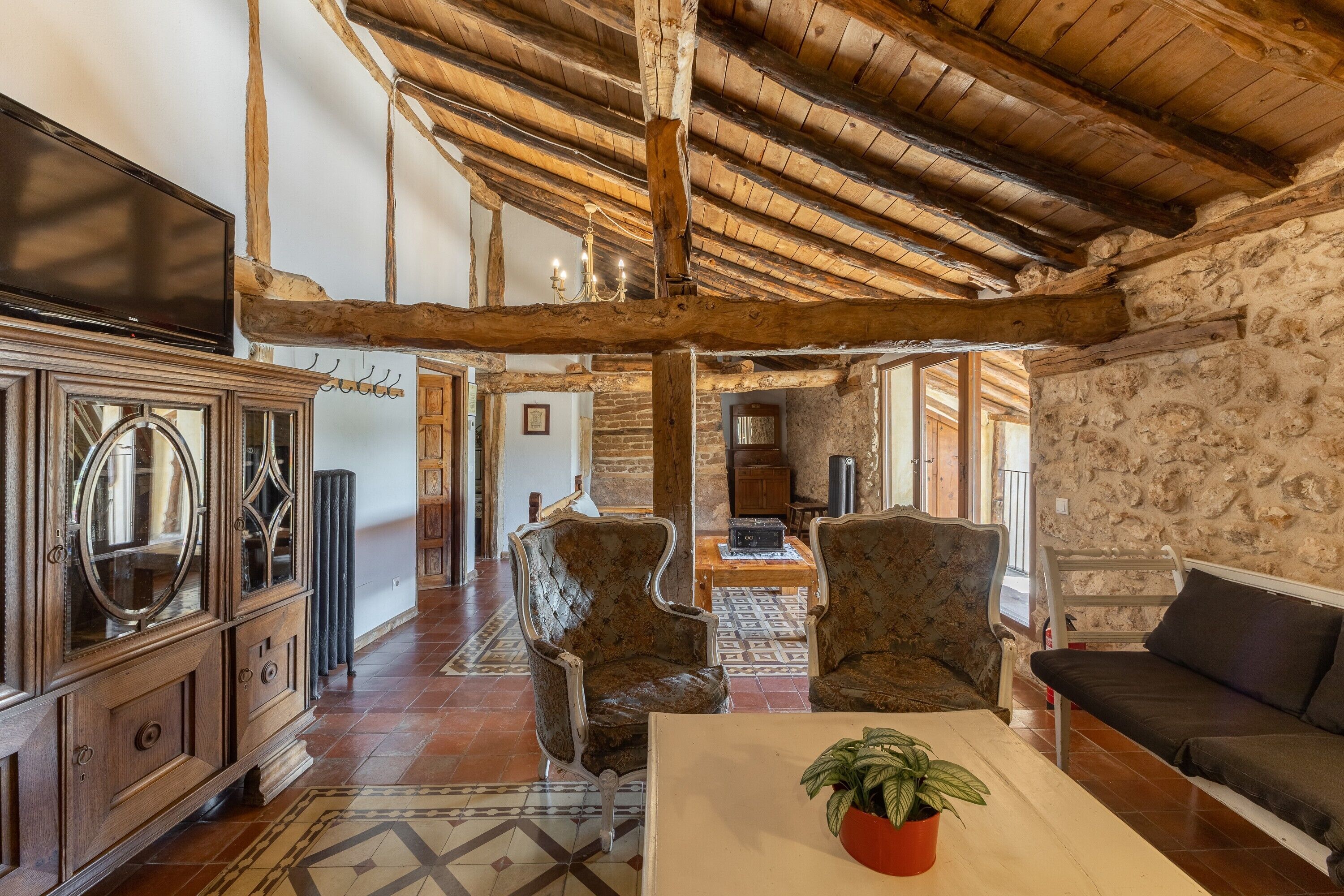 Un interior rústico con vigas de madera a la vista, una pared de piedra, un aparador de madera y un sofá.