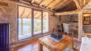 Un interior rústic amb parets de pedra, bigues de fusta, una llar de foc, una finestra gran i una biblioteca.