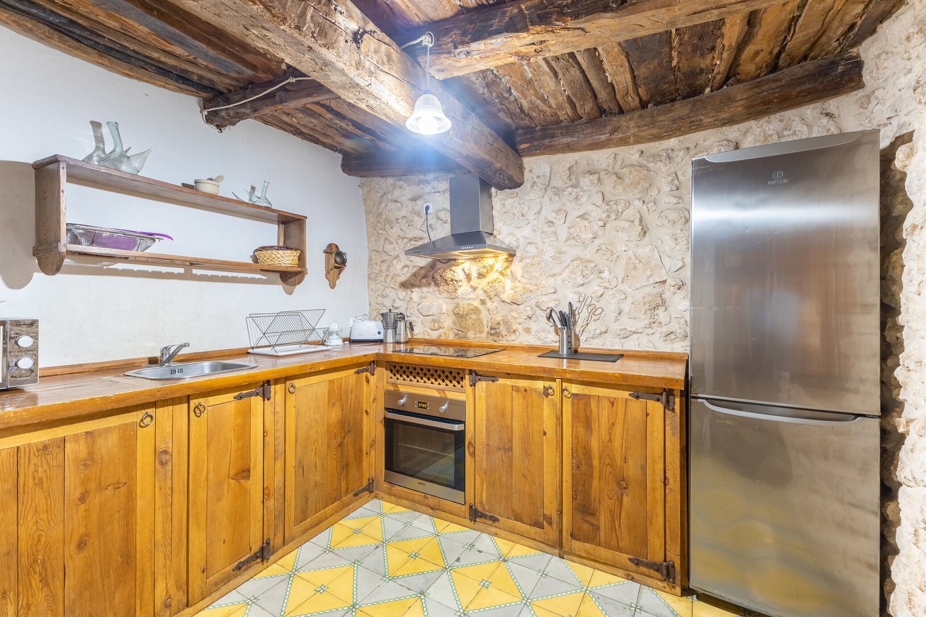 Una cocina con armarios de madera, un refrigerador de acero inoxidable, una pared de piedra y un piso de baldosas amarillo y blanco.