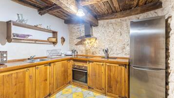 Una cocina con armarios de madera, un refrigerador de acero inoxidable, una pared de piedra y un piso de baldosas amarillo y blanco.