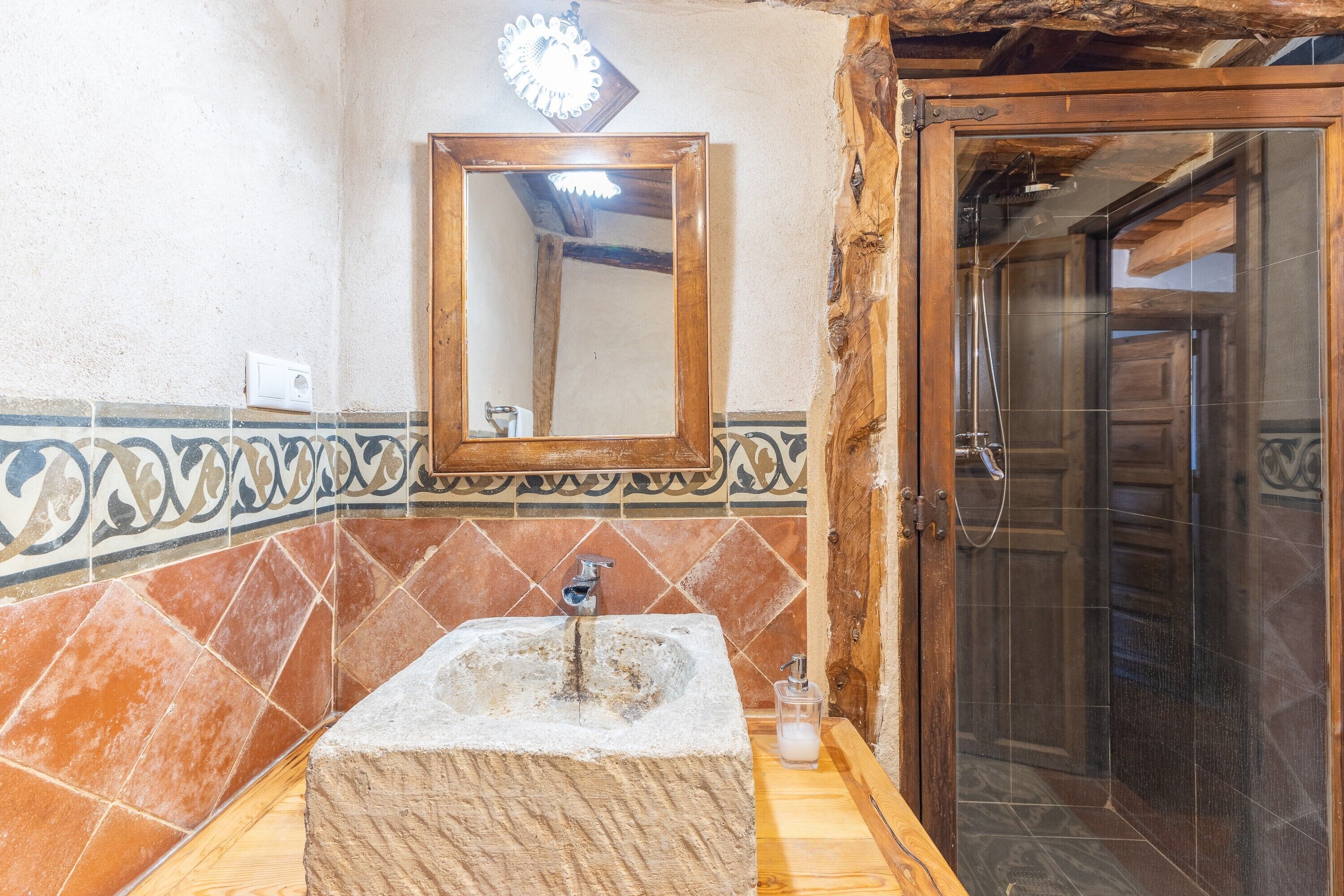 A bathroom with a stone sink, a mirror, and a shower area.