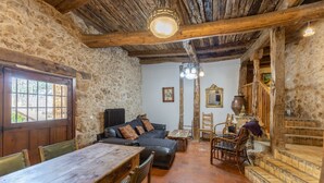 Un interior rústic amb parets de pedra, sostre de fusta, taula de dinar, sofà i una escala.
