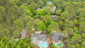 Vista aérea de una zona residencial con varias casas rodeadas de abundante vegetación, una piscina y vistas al océano.