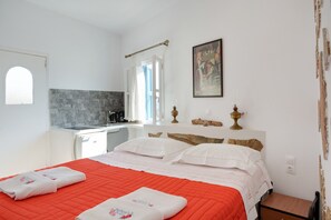 Une chambre avec un lit, une fenêtre, un tableau et un coin cuisine.