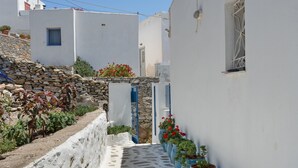 A narrow alleyway with white buildings, stone walls, and potted plants.