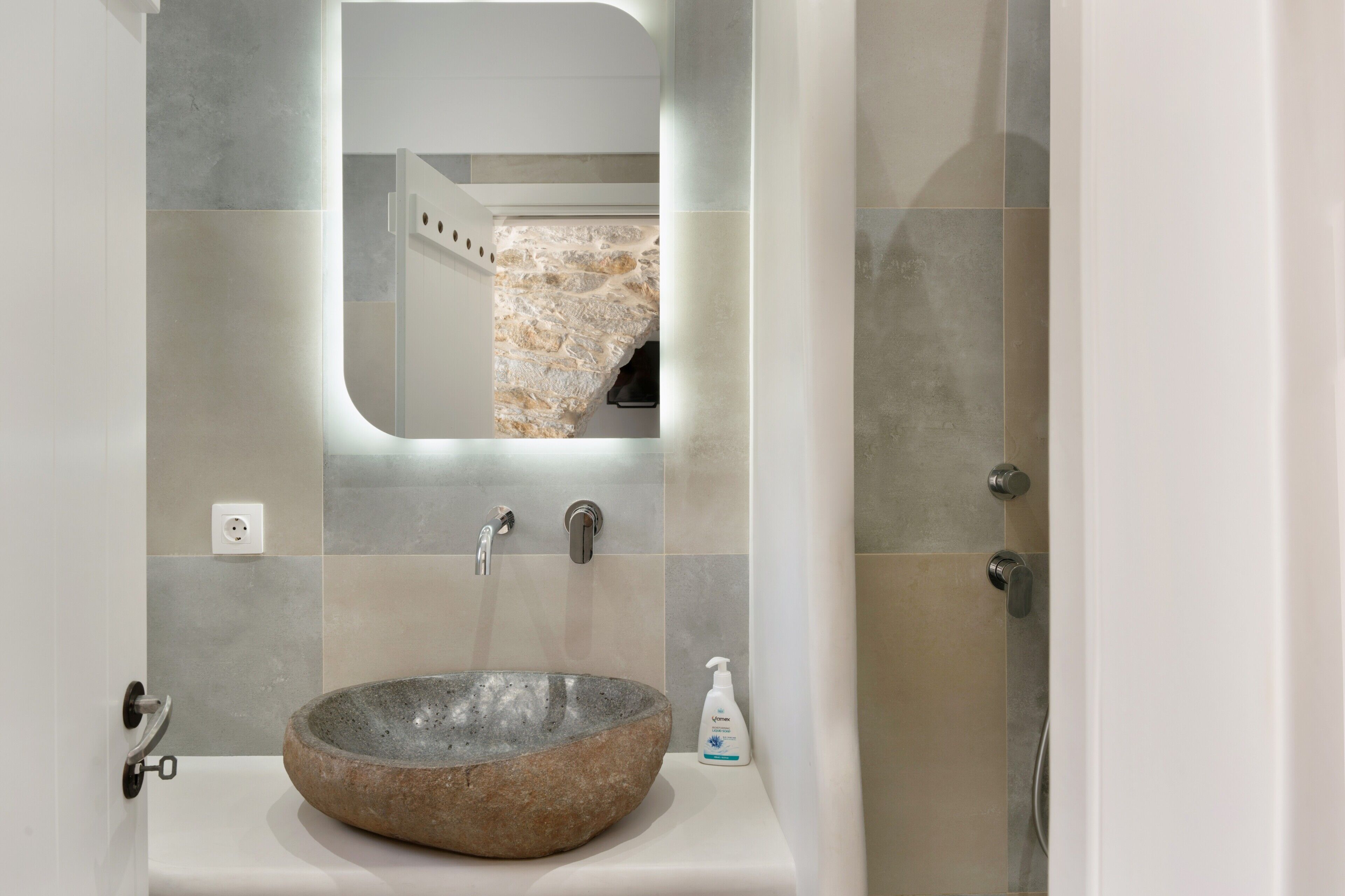 A bathroom with a stone sink, a mirror, and a shower.