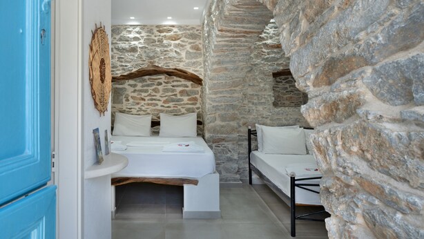 Une chambre aux murs de pierre, avec un lit, un canapé et une porte bleue.