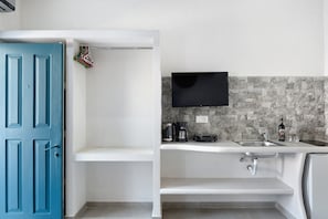 A compact kitchen with a blue door, a mounted TV, and a stone backsplash. - Studio Apartment 'Politimi  N1' with Mountain View, Wi-Fi and Air Conditioning (Amorgos)