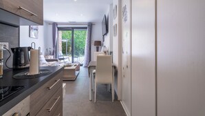 A modern kitchen with a coffee maker, a dining area with a table and chairs, and a view of the outdoors through a glass door. - Escape and serenity at Studio Le Partegal with shared pool, Wi-Fi and air conditioning (La Valette-du-Var)