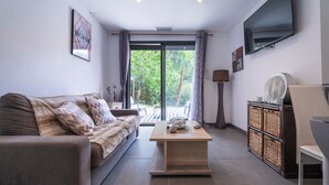 A modern living room with a sofa, a coffee table, a TV, and a view through a glass door. - Escape and serenity at Studio Le Partegal with shared pool, Wi-Fi and air conditioning (La Valette-du-Var)