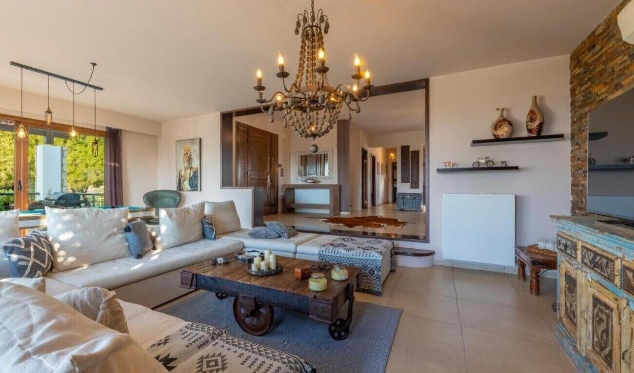 Una sala de estar moderna con candelabro, sofá, mesa de centro y vistas al exterior.