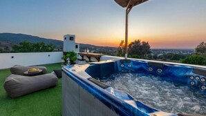 Un bain à remous sur un toit-terrasse, offrant une vue sur le coucher de soleil et les collines lointaines.