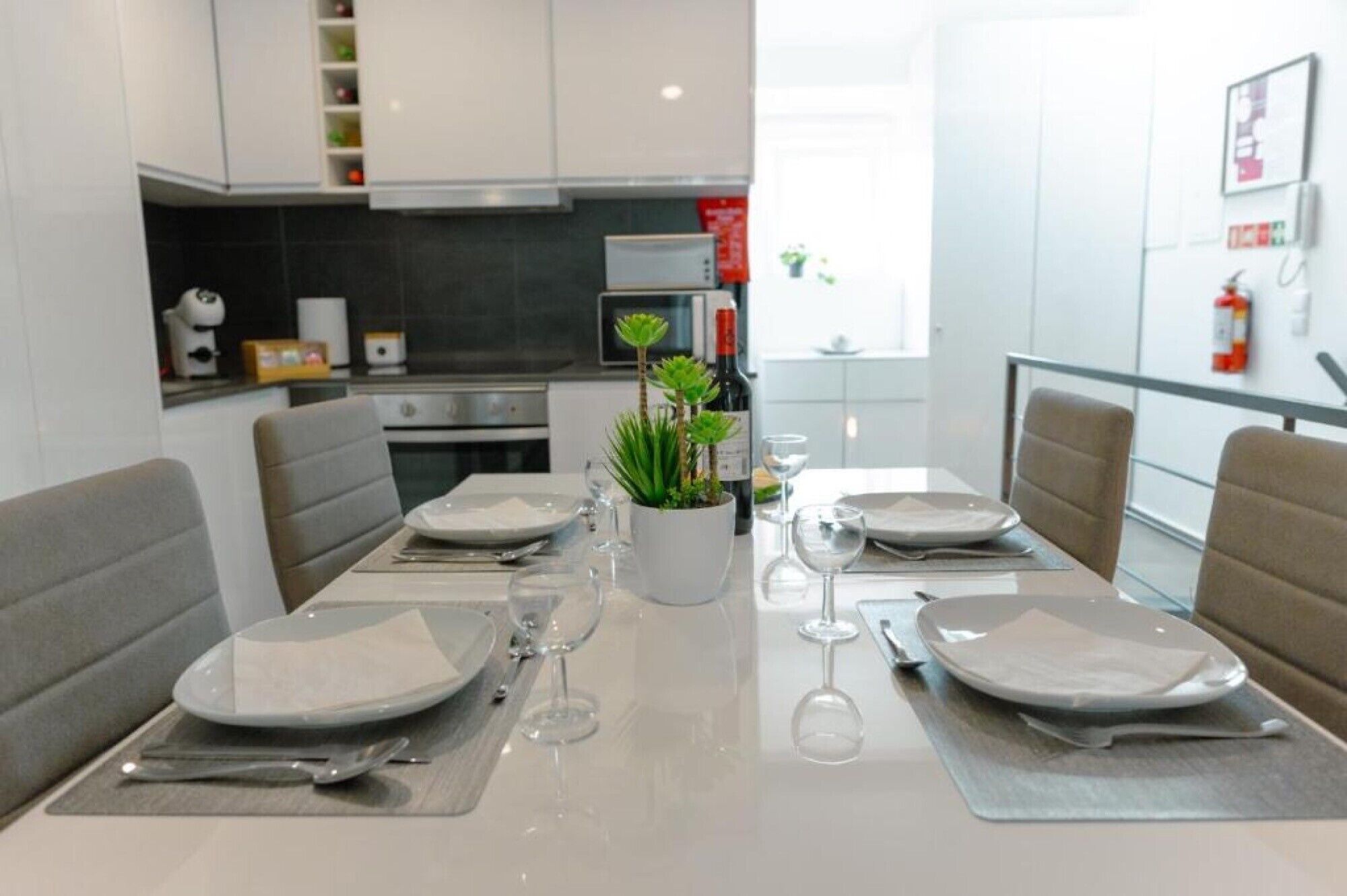 A modern dining area with a table set for four, a potted plant, and a wine bottle.