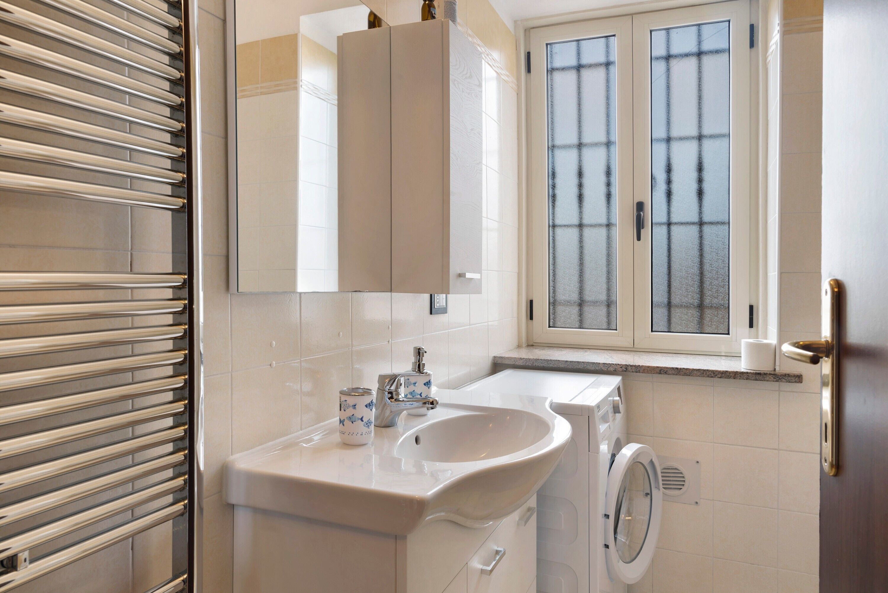 A bathroom with a sink, mirror, window, and a washing machine.