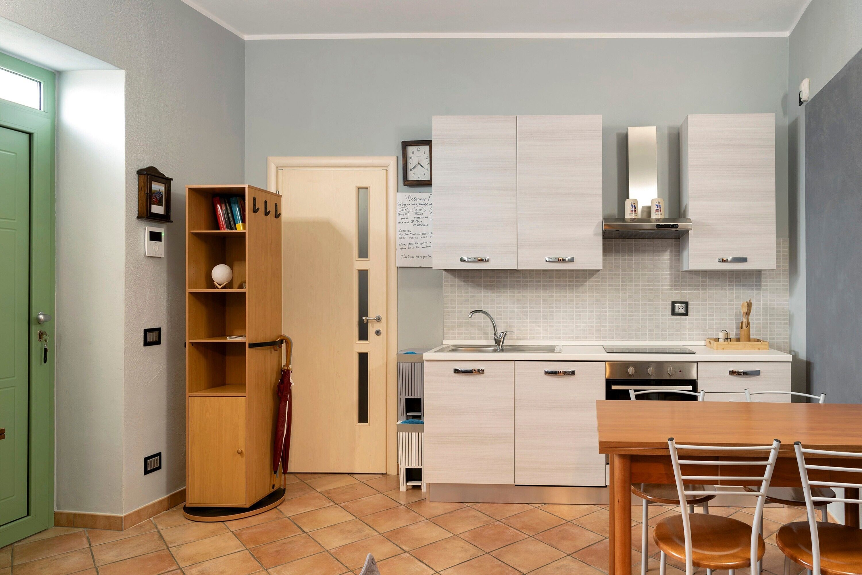 A compact kitchen with white cabinets, a wooden dining table, and a green door.