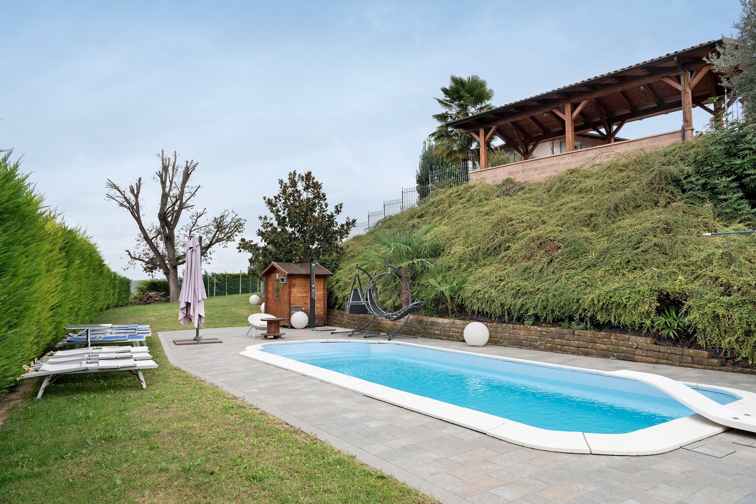 A swimming pool with a wooden deck, a small wooden structure, and a covered area with a view of the surrounding landscape.