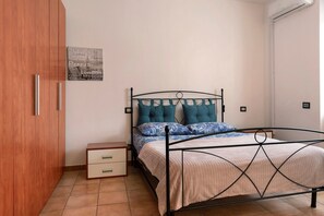 Una camera da letto con un letto a struttura metallica, un armadio in legno, un comodino con cassetti e un condizionatore d'aria a parete.