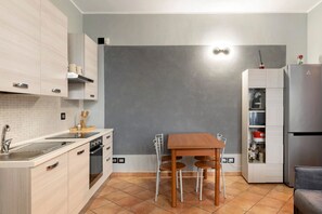 Una cucina moderna con mobili in legno chiaro, forno integrato, frigorifero in acciaio inox e zona pranzo con tavolo e sedie in legno.