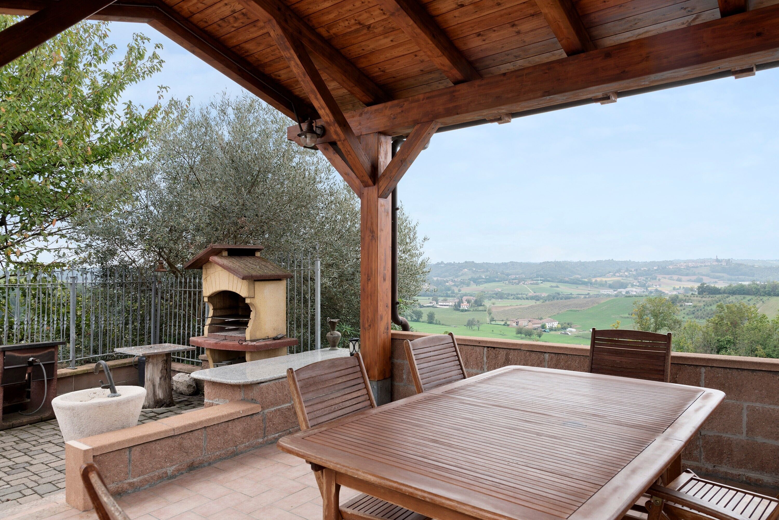 Une terrasse extérieure avec une table et des chaises en bois, un évier en pierre et un four en briques.