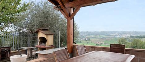 Une terrasse extérieure avec une table et des chaises en bois, un évier en pierre et un four en briques.