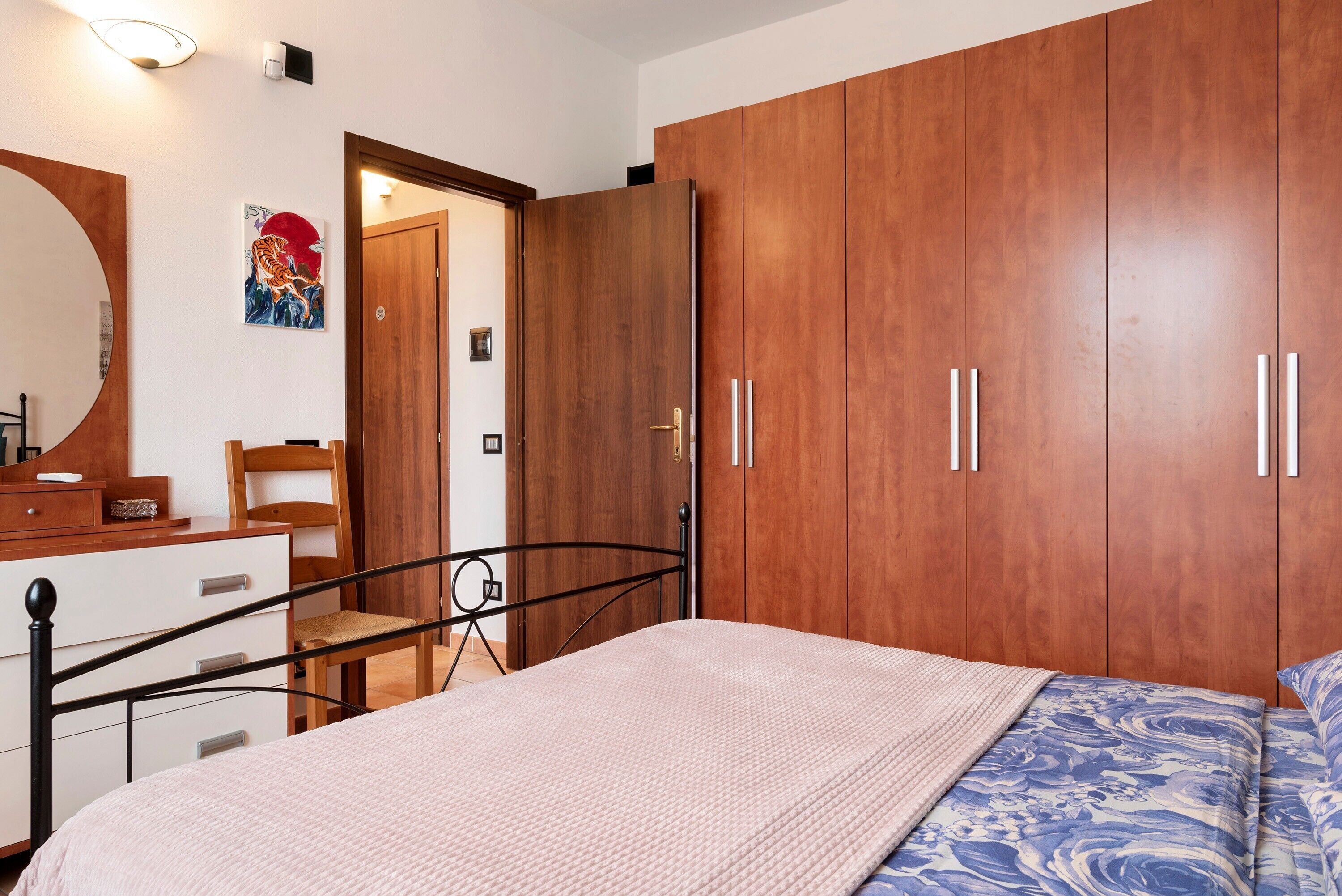 Ein Schlafzimmer mit einem Bett, einem Holzschrank, einem Stuhl, einem Schreibtisch und einem Spiegel.